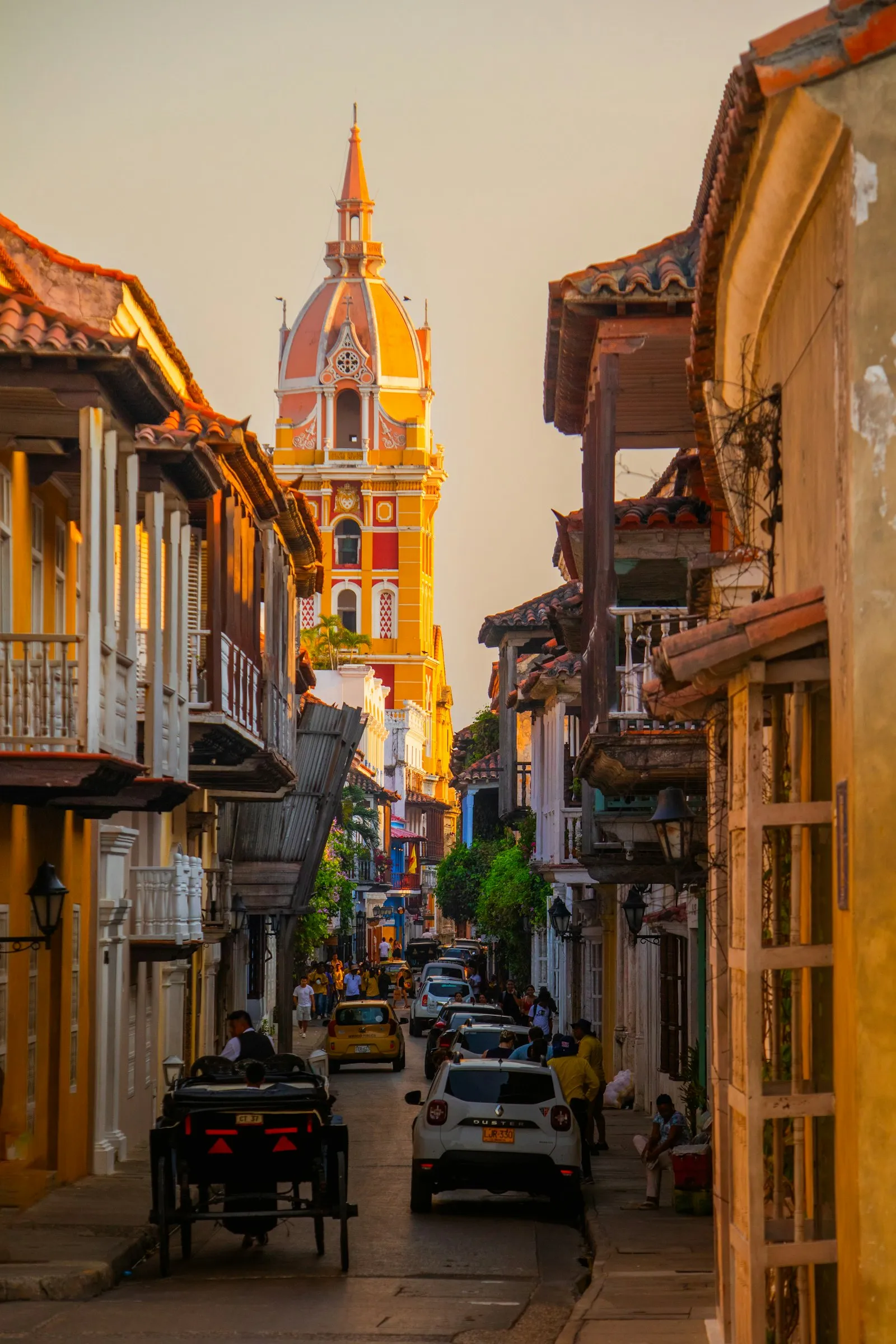 Una calle de Cartagena iluminada de dorado al atardecer, con una torre de iglesia a lo lejos