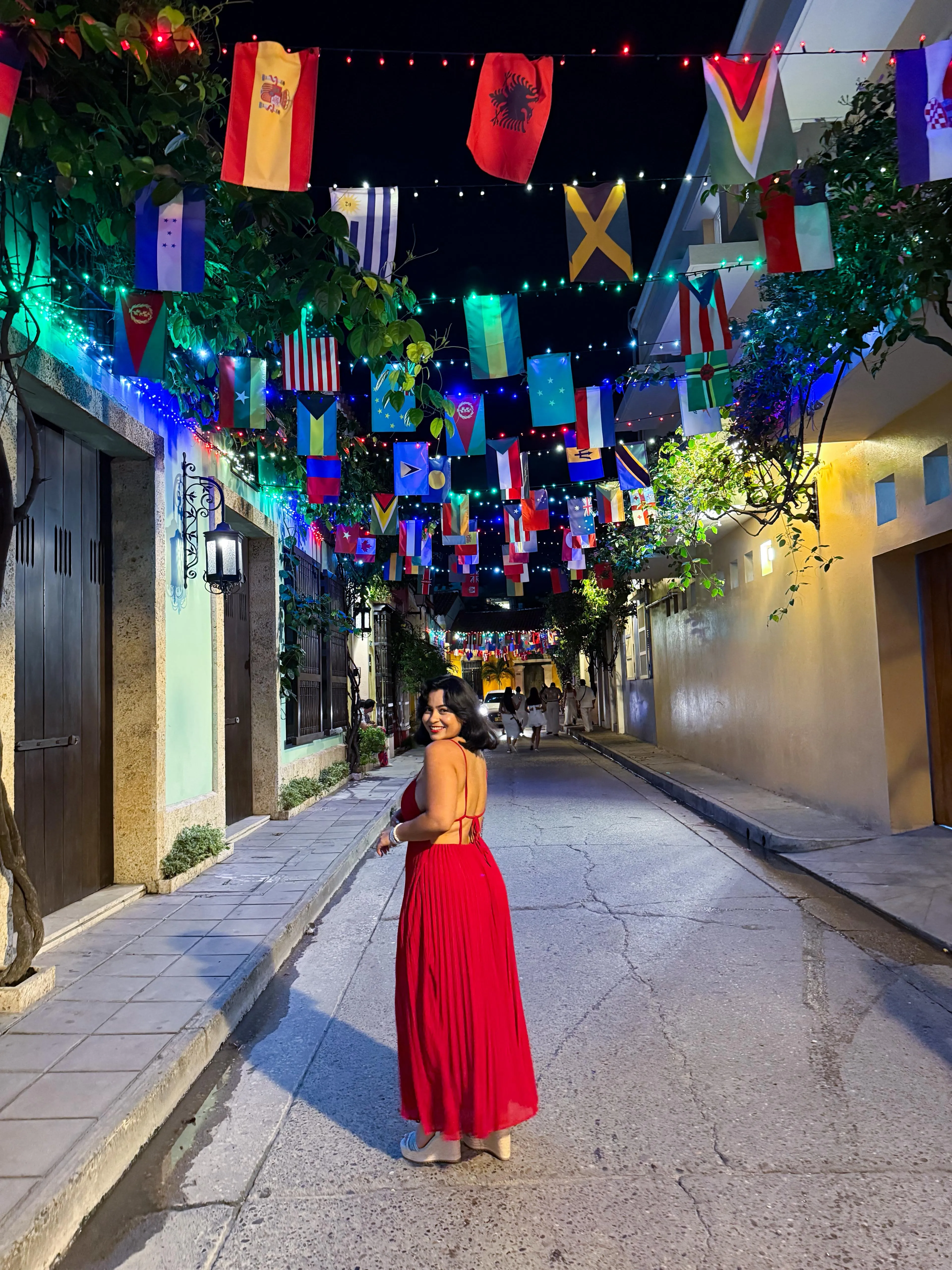 Una mujer con un vestido rojo mira hacia atrás en un callejón de Cartagena iluminado con banderas de noche